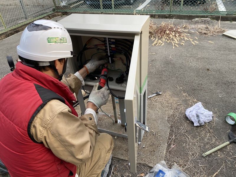 屋外の制御盤で結線作業をする当社社員